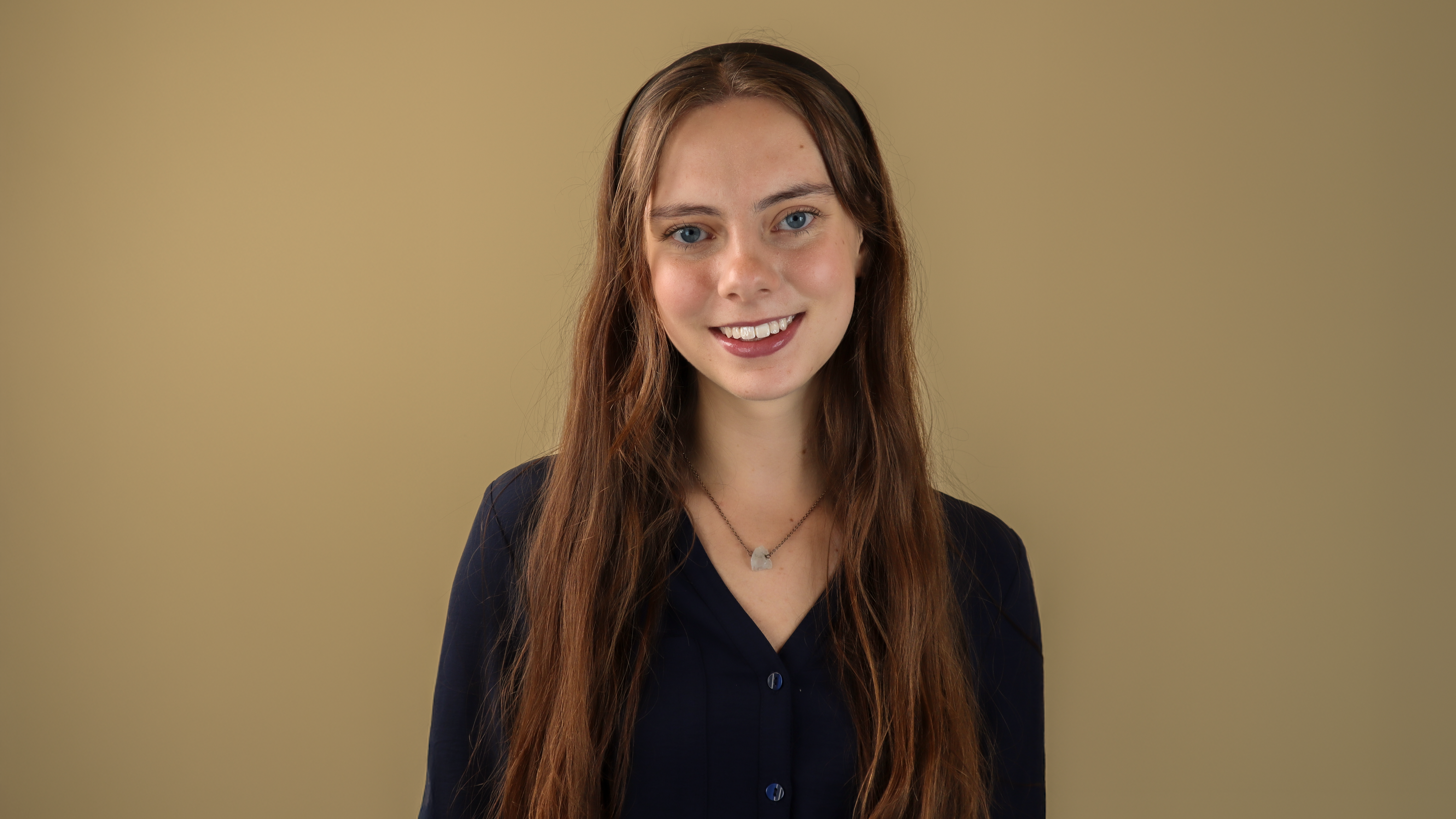 Evalyn Green smiles while wearing a black sweater and necklace in front of a beige background. Evalyn Green smiles while wearing a black sweater and necklace in front of a beige background.